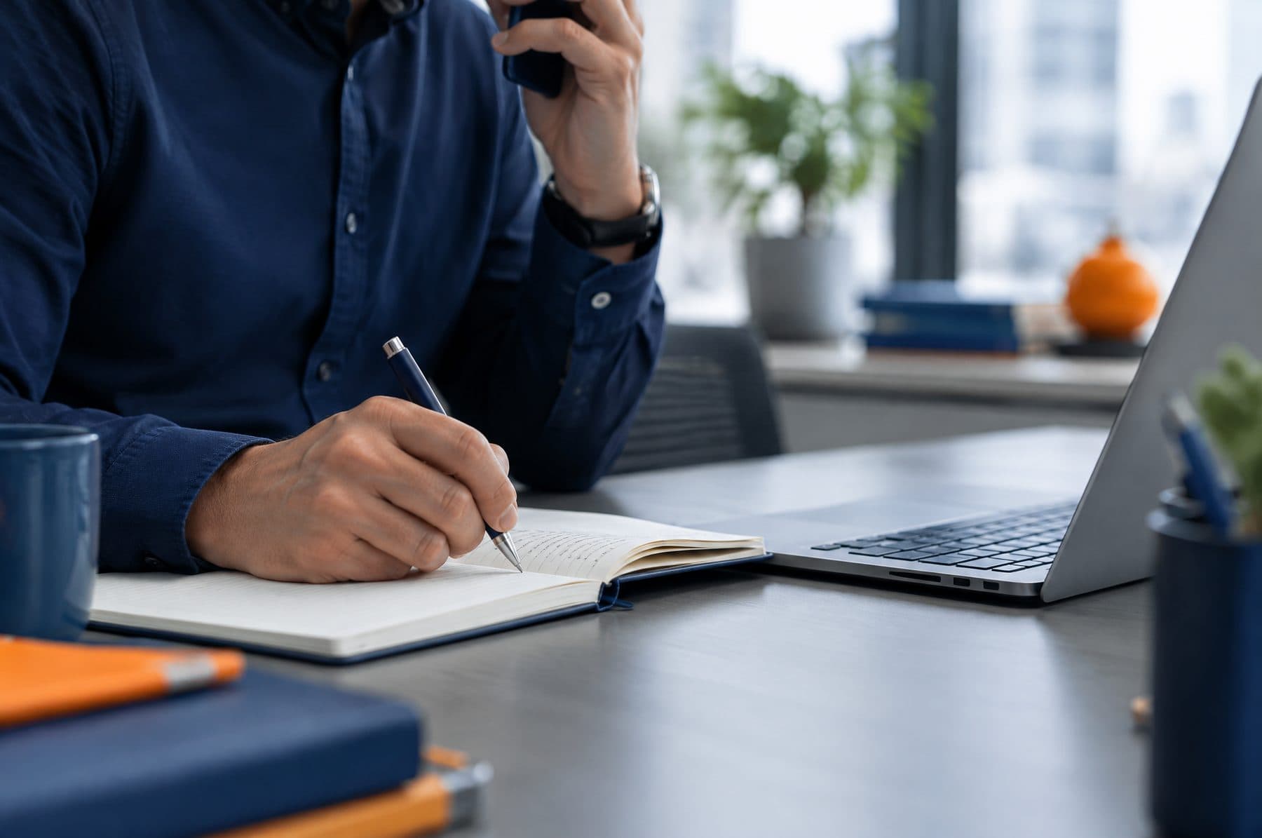 A recruitment consultant on a phone call writing notes beside a laptop