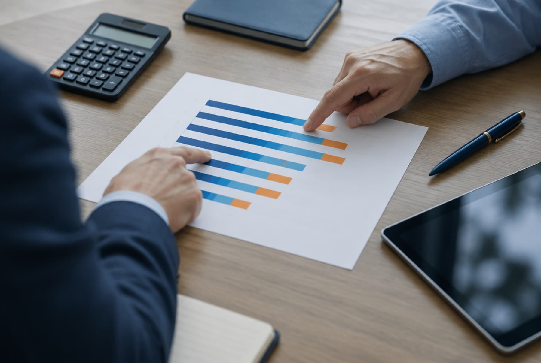 Two colleagues' hands pointing at a printed chart of pay bands beside a calculator