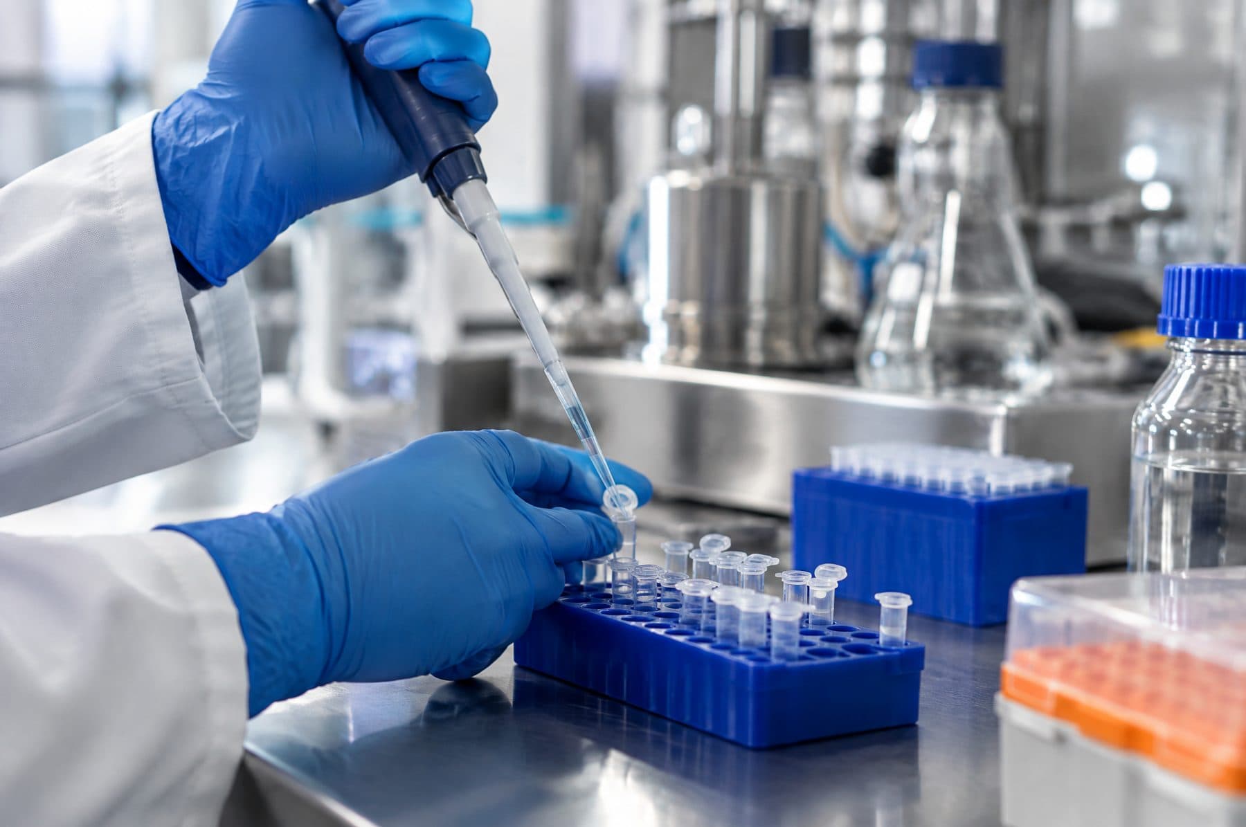 Gloved hands using a pipette over sample tubes in a pharmaceutical quality control laboratory